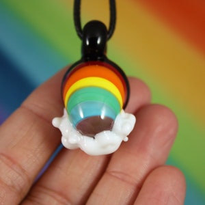 May include: A rainbow glass pendant with a white cloud design. The pendant is on a black cord.