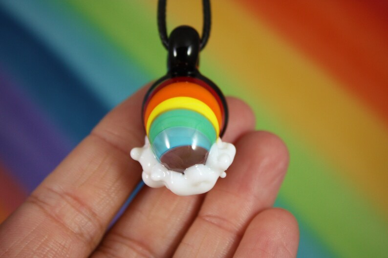 May include: A rainbow glass pendant with a white cloud design. The pendant is on a black cord.