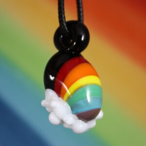 May include: A rainbow glass pendant with a black cord and a white cloud charm. The pendant features a rainbow with red, orange, yellow, green, blue, and purple stripes.