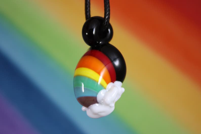 May include: A rainbow glass pendant with a white cloud design, hanging from a black cord.