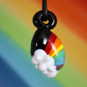 May include: A glass pendant with a rainbow design and a white cloud. The pendant is black on the top and has a black cord.