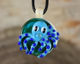 May include: A blue glass octopus pendant with white eyes and blue dots on its tentacles. The pendant is hanging from a black cord.