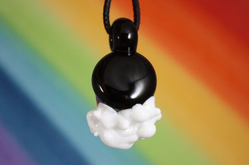May include: A black glass pendant with a white glass cloud design. The pendant is hanging from a black cord.