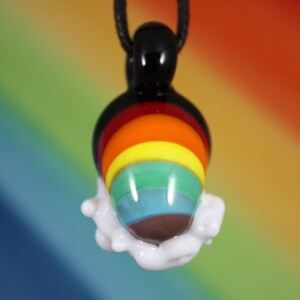 May include: A rainbow glass pendant with a white cloud-like design around the bottom. The pendant is hanging from a black cord.