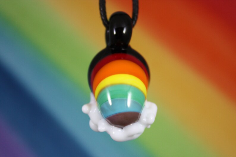 May include: A rainbow glass pendant with a white cloud-like design around the bottom. The pendant is hanging from a black cord.
