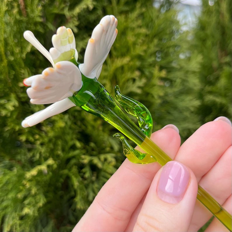K&ouml;nnte beinhalten: Eine zarte Glasblume mit wei&szlig;en Bl&uuml;tenbl&auml;ttern und einem gr&uuml;nen Stiel. Die Blume ist handgefertigt und hat ein realistisches Aussehen.