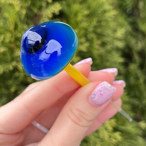 May include: A blue glass mushroom with a yellow stem. The mushroom is shaped like a dome and has a smooth, shiny surface.
