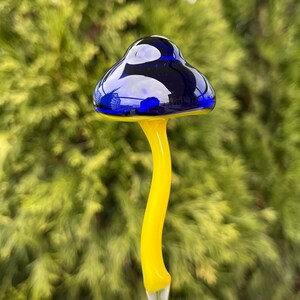 May include: A glass mushroom garden stake with a blue cap and a yellow stem.
