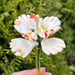 K&ouml;nnte beinhalten: Eine wei&szlig;e Glasblume mit roten, orangen und gelben Akzenten. Die Blume ist handf&ouml;rmig mit f&uuml;nf Fingern. Der Stiel ist aus gr&uuml;nem Glas.