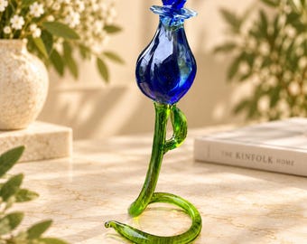 May include: A handcrafted glass sculpture of a flower featuring a deep blue bulbous bloom with a small blue petal detail at the top. The stem is made of translucent green glass, curving downward to form a circular base that supports the upright flower.