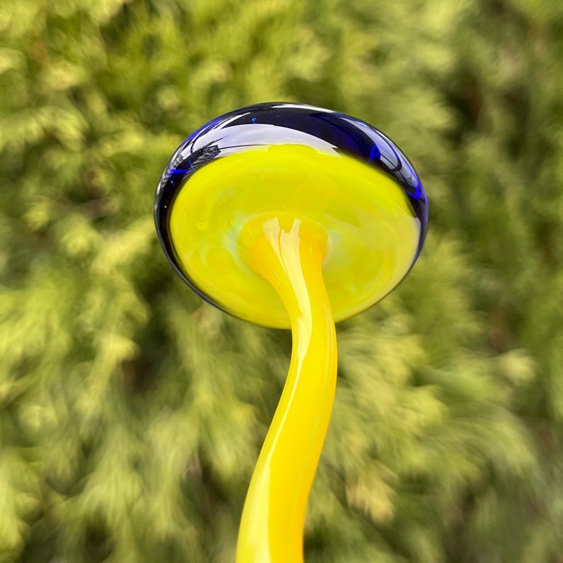 May include: A glass mushroom sculpture with a yellow stem and a blue and yellow cap.