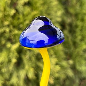 May include: A blue glass mushroom with a yellow stem. The mushroom is sitting on a green background.