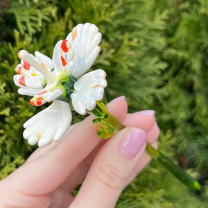 K&ouml;nnte beinhalten: Eine wei&szlig;e Glasblume mit roten und gelben Akzenten. Die Blume hat einen gr&uuml;nen Stiel.