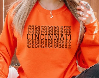 May include: Orange sweatshirt with the word "Cincinnati" repeated three times in black outlined text.
