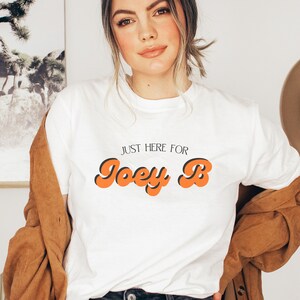 May include: White t-shirt with the text "Just here for Joey B" in orange and black retro font.