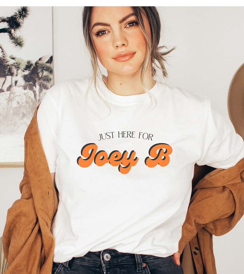 May include: White t-shirt with the text "Just here for Joey B" in orange and black retro font.