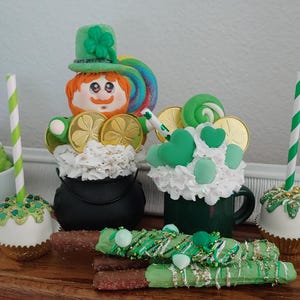 May include: A collection of St. Patrick's Day themed treats, including a leprechaun figurine, a green and white cupcake, a green and white mug, and a chocolate-covered pretzel. The treats are decorated with shamrocks, gold coins, and green sprinkles.