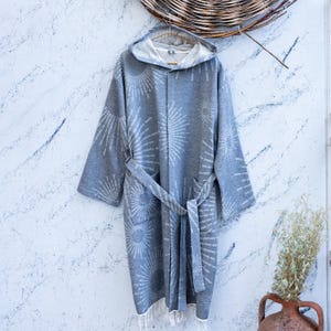 May include: A gray hooded bathrobe with a white sunburst pattern. The robe has a tie belt and a fringe trim.