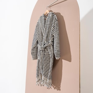 May include: Black and white waffle weave hooded robe with a self-tie belt and fringe trim.
