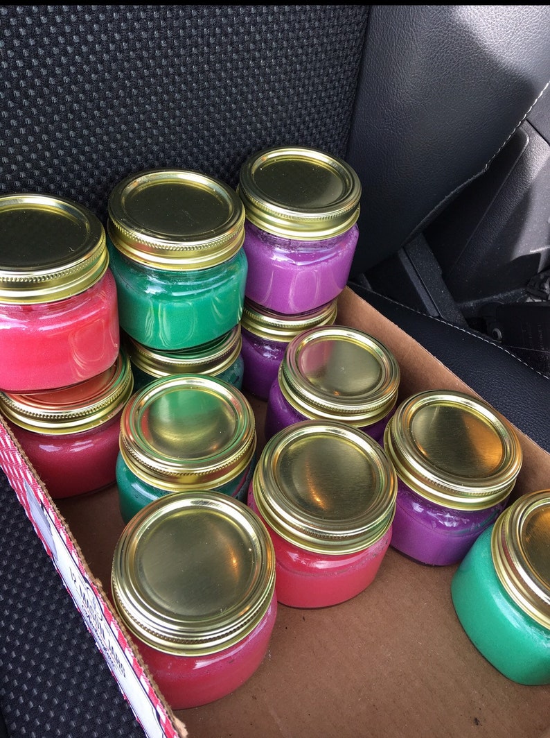 May include: A box filled with small glass jars with gold lids. The jars are filled with different colored wax, including red, purple, and green.