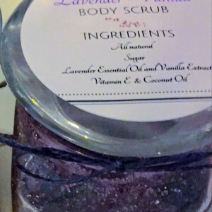 May include: A glass jar filled with a lavender and vanilla scented body scrub. The label reads "Lavender-Vanilla Body Scrub" and lists the ingredients as "All natural, Sugar, Lavender Essential Oil and Vanilla Extract, Vitamin E & Coconut Oil".