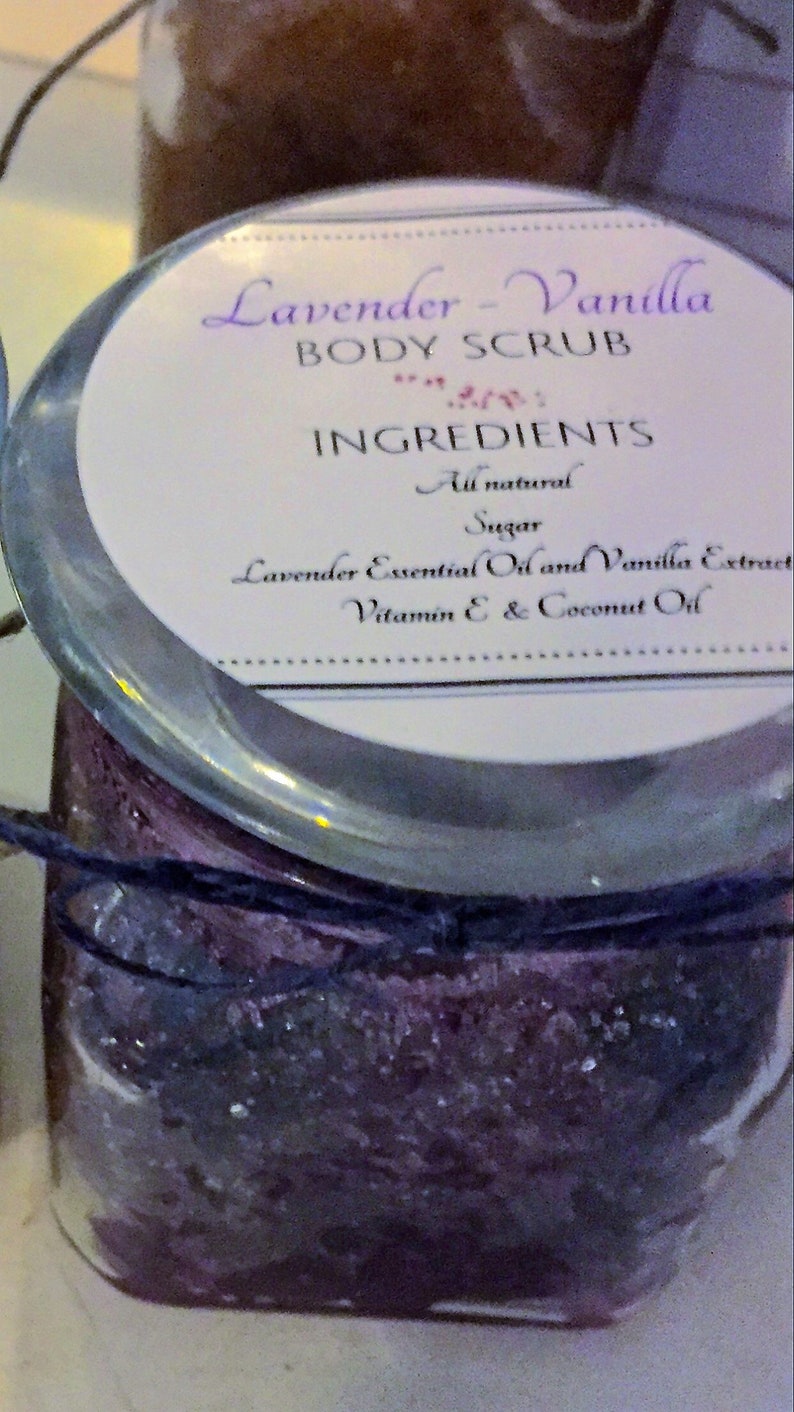 May include: A glass jar filled with a lavender and vanilla scented body scrub. The label reads "Lavender-Vanilla Body Scrub" and lists the ingredients as "All natural, Sugar, Lavender Essential Oil and Vanilla Extract, Vitamin E & Coconut Oil".