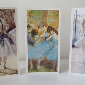 May include: Three rectangular art prints depicting ballet dancers. The prints show Impressionist-style paintings of ballerinas in different poses, with soft colours and delicate brushstrokes. The prints are displayed on a white surface.