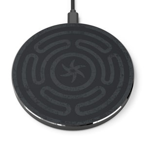 Puede incluir: Una base de carga inalámbrica negra con un diseño circular que presenta una estrella estilizada en el centro. La base de carga tiene una superficie texturizada.