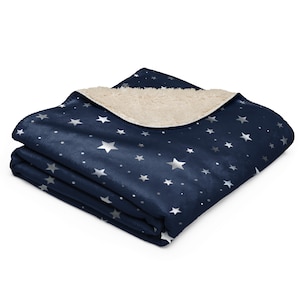 May include: A folded navy blue blanket with a silver star pattern. The blanket has a soft, plush texture and a cream-colored sherpa lining. The stars vary in size and are scattered across the surface.