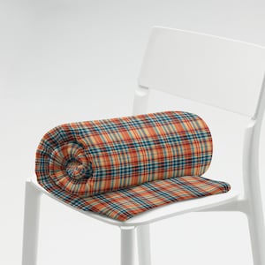 May include: A rolled up plaid blanket in shades of orange, blue, and beige, sitting on a white chair.