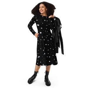May include: A black midi dress with a white star print. The dress has long sleeves and a flared skirt. The model is wearing black ankle boots.