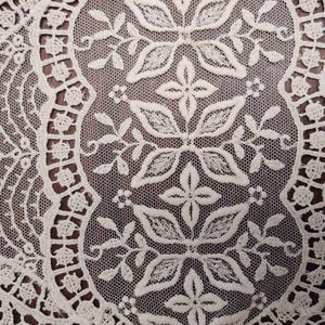 May include: White lace fabric with a delicate floral pattern. The lace has a circular design with a repeating pattern of flowers and leaves.