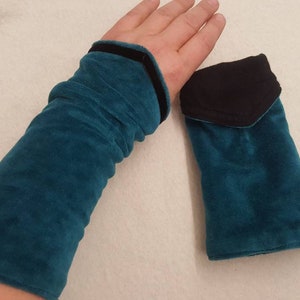 May include: A pair of teal blue velvet arm warmers with black trim. One arm warmer has a black velvet pocket.