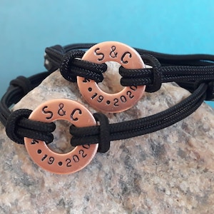 May include: Two black paracord bracelets with copper rings. The rings are engraved with "S&C" and the dates "4.19.2020".