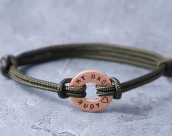 May include: A green paracord bracelet with a copper charm that reads "MY DAD RUDY" with a heart symbol.