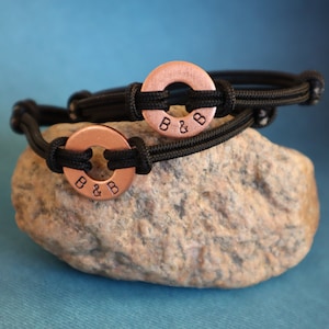May include: Two black paracord bracelets with copper rings. The rings have the initials "B & B" engraved on them.