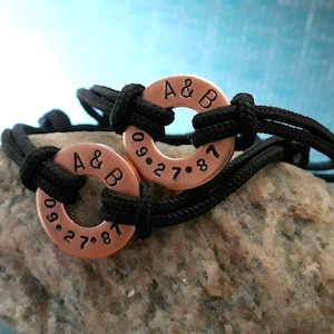 May include: Two black cord bracelets with copper rings. The rings are engraved with "A & B" and the date "09.27.87".