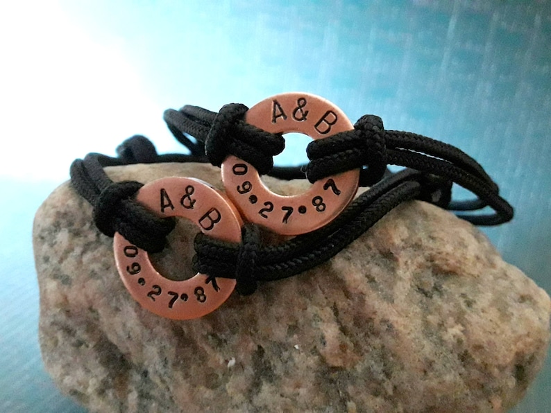 May include: Two black cord bracelets with copper rings. The rings are engraved with "A & B" and the date "09.27.87".