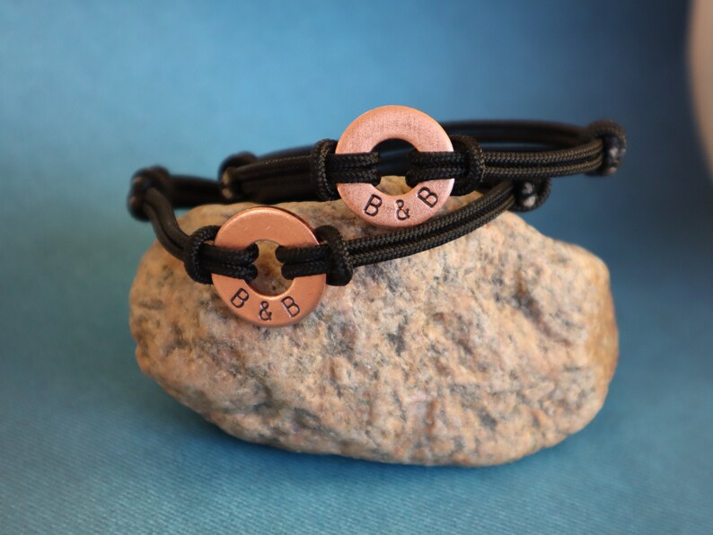 May include: Two black paracord bracelets with copper rings. The rings have the initials "B & B" engraved on them.