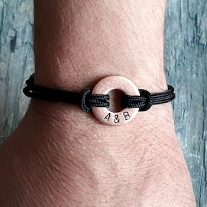 May include: A black paracord bracelet with a copper ring charm engraved with the initials "A & B".