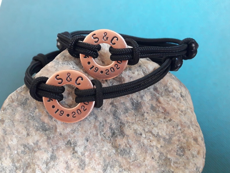 May include: Two black paracord bracelets with copper rings. The rings are engraved with "S&C" and the dates "4.19.2020".