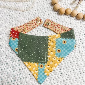 Peut inclure: Un bandana pour chien en patchwork avec un motif floral et de tournesols. Le bandana présente un panneau central vert avec des points blancs et est bordé de tissu floral jaune, bleu et rouge. Les sangles de cou réglables sont beiges avec des accents floraux rouges.