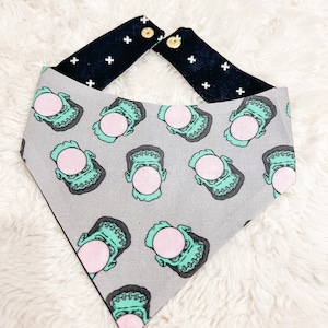 May include: A gray bandana with a black and white patterned trim. The bandana features a repeating pattern of green Frankenstein faces blowing pink bubble gum.