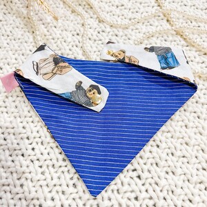 May include: A blue and white striped dog bandana with two matching collar attachments. The attachments feature a repeating pattern of teddy bears in various outfits. The bandana is made of fabric.