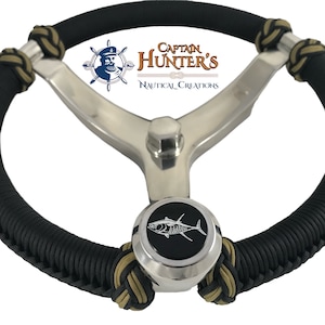 May include: Black and gold braided steering wheel cover with a silver steering wheel and a silver knob with a tuna fish graphic. The knob has the text "Captain Hunter's Nautical Creations".