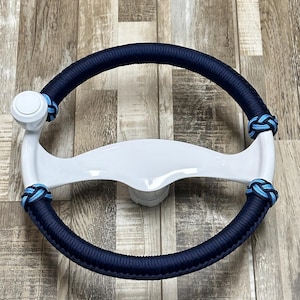 May include: White steering wheel with a blue and light blue rope wrap. The wheel has a white knob on the left side.