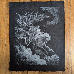 May include: A rectangular black fabric patch featuring a white screen-printed illustration of a cloaked figure riding a horse through clouds, accompanied by winged creatures. The artwork includes the signature G. Doré and the name H. Pisan.