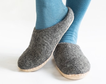 May include: A pair of gray felt slippers with a light brown sole. The slippers are worn by a person wearing blue socks.