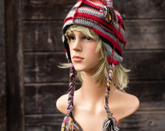 May include: A red, black, and gray striped knit hat with long braided cords. The hat has a fold-down ear flap and is worn on a mannequin.