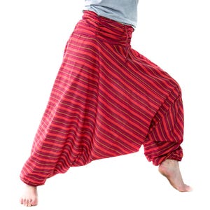May include: Red striped harem pants with a gathered waistband. The pants have a loose, flowing design and are made of a lightweight fabric. The stripes are a mix of red and gold.
